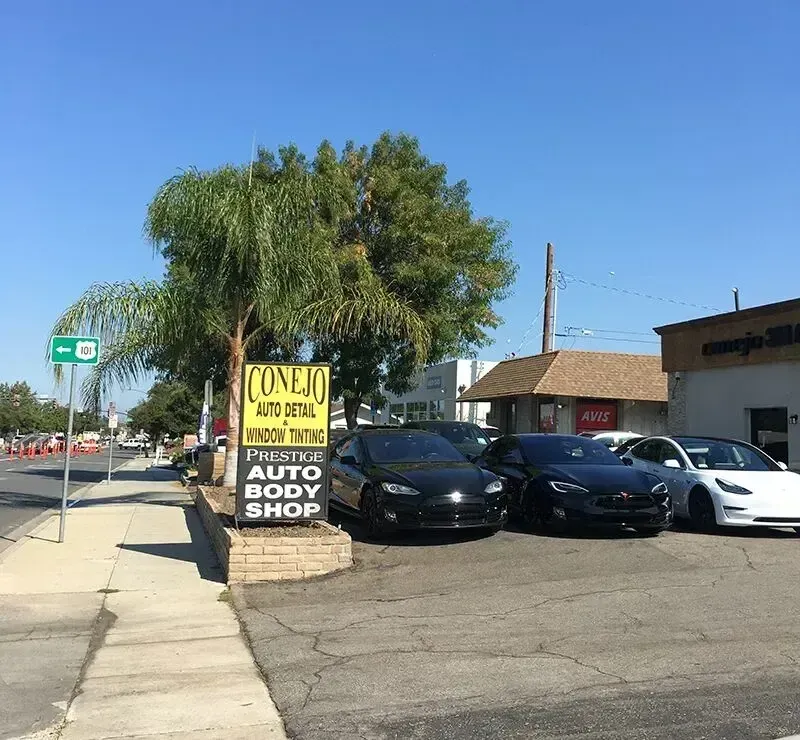 Auto body shop sign beside parked cars on a sunny street corner