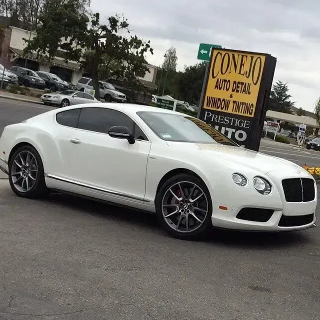White luxury coupe parked outdoors beside a sign advertising car detailing services.