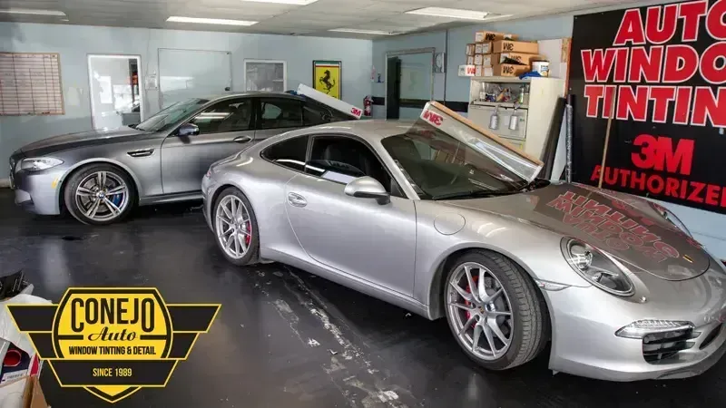 Two silver sports cars inside an auto window tinting shop with bold red signage.