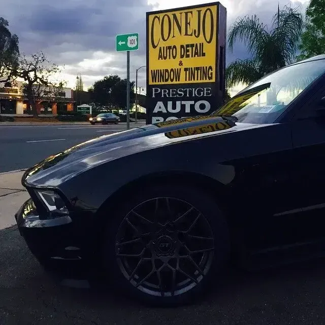 Dark car parked near a Conejo Auto Detail and window tinting sign at dusk