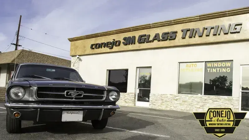 Classic black Mustang parked outside Conejo’s Glass Tinting shop on a sunny street.