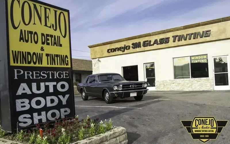 Conelo auto detailing and window tinting shop with a black SUV parked outside and large roadside signboard