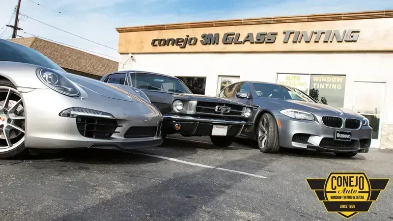 Three sports cars parked outside Conejo SM Glass Tinting shop with a yellow logo sign.