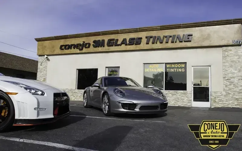 Two sports cars parked outside Conejo Smog Glass Tinting shop with signage on the building