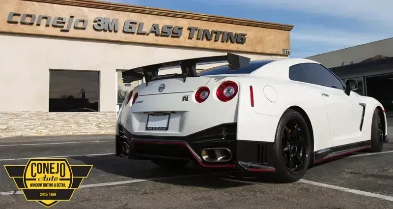 White Nissan GT-R parked outside Conejo SM Glass Tinting shop, rear three-quarter view, black wheels and spoiler