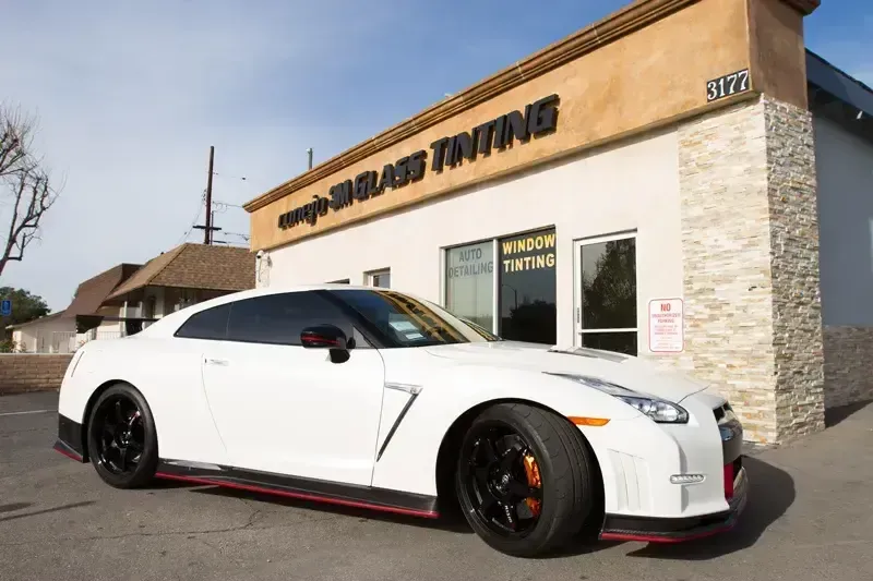 White sports car with black and red accents parked outside a tuning shop