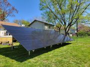 A large solar panel is sitting in the grass in front of a house.