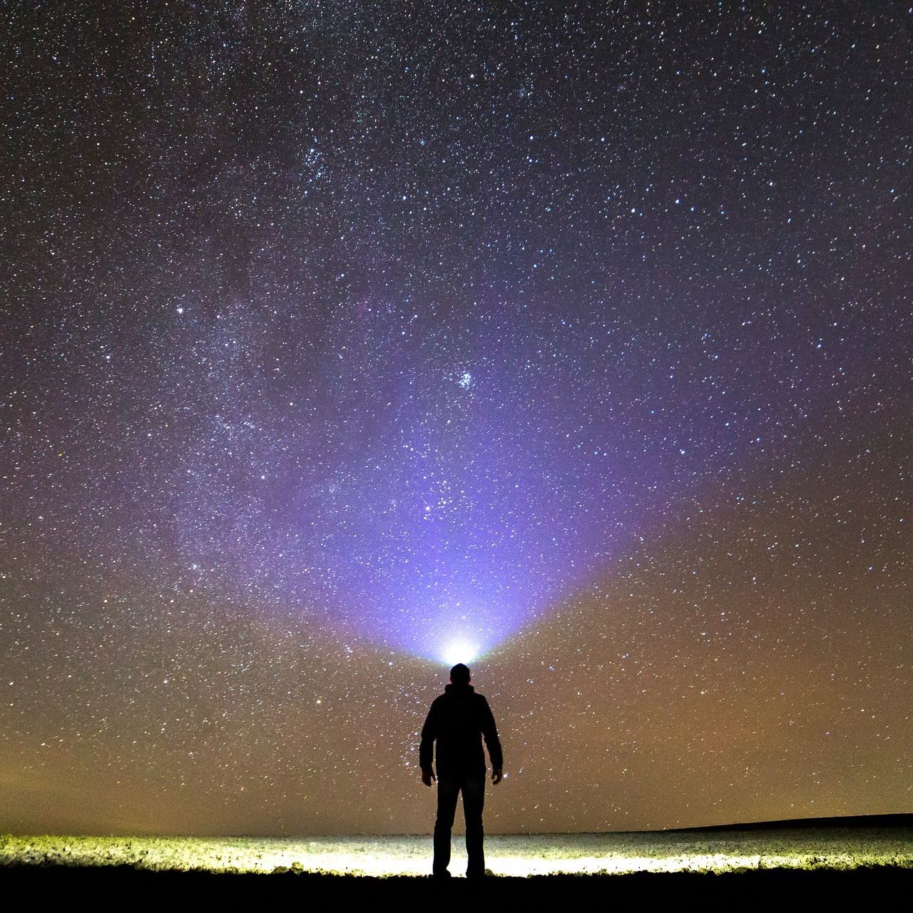 A person is holding a flashlight in front of a starry sky