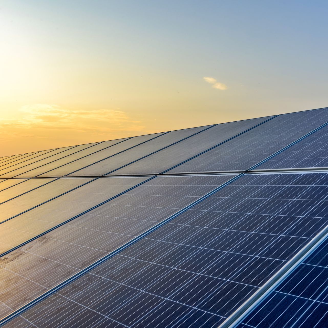 A row of solar panels on a roof at sunset