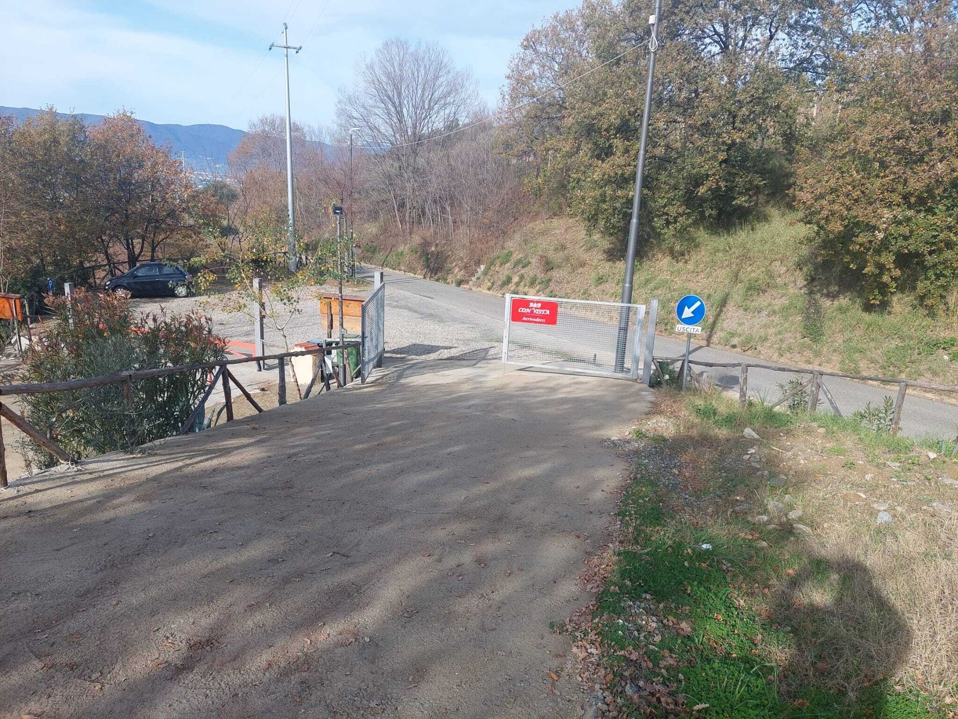 Una strada sterrata con una recinzione e un cartello di divieto di accesso