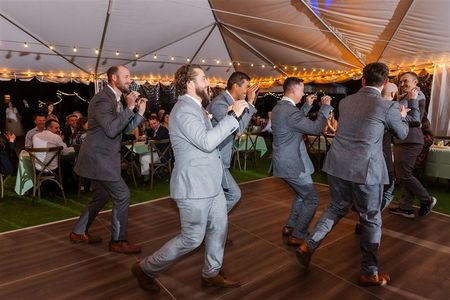 A group of men in suits are dancing on a dance floor under a tent.