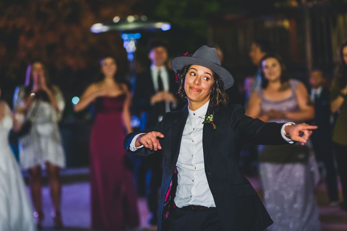 A woman in a suit and hat is dancing at her wedding reception.