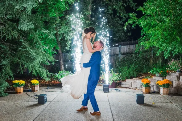 A bride and groom are dancing in front of a fireworks display.