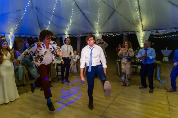 A group of people are dancing in a tent at a wedding reception.