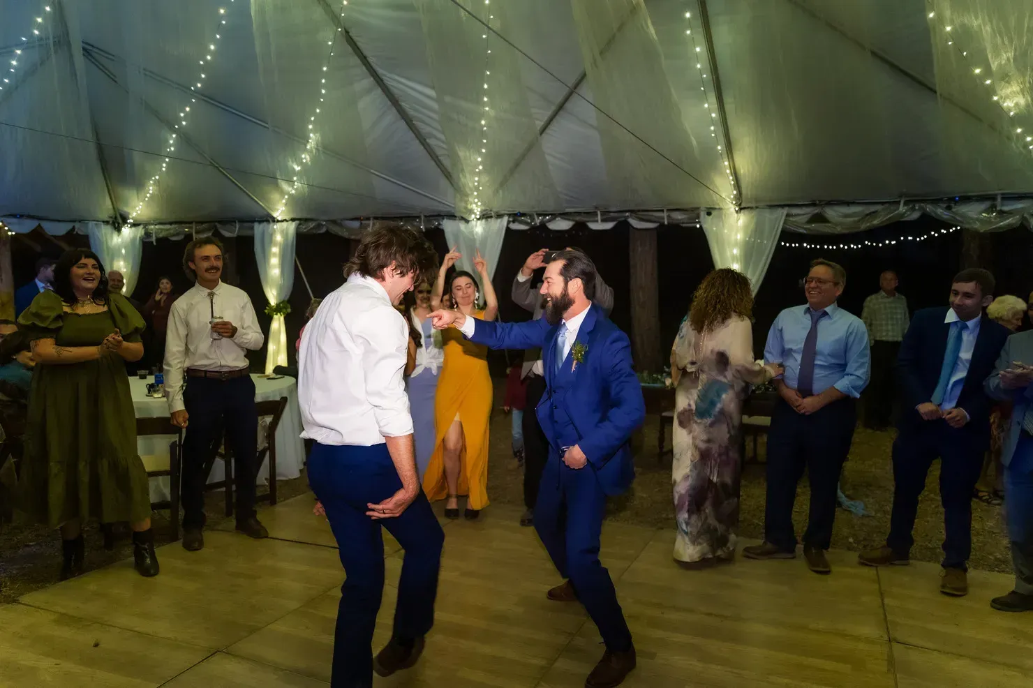 A group of people are dancing under a tent at a wedding reception.