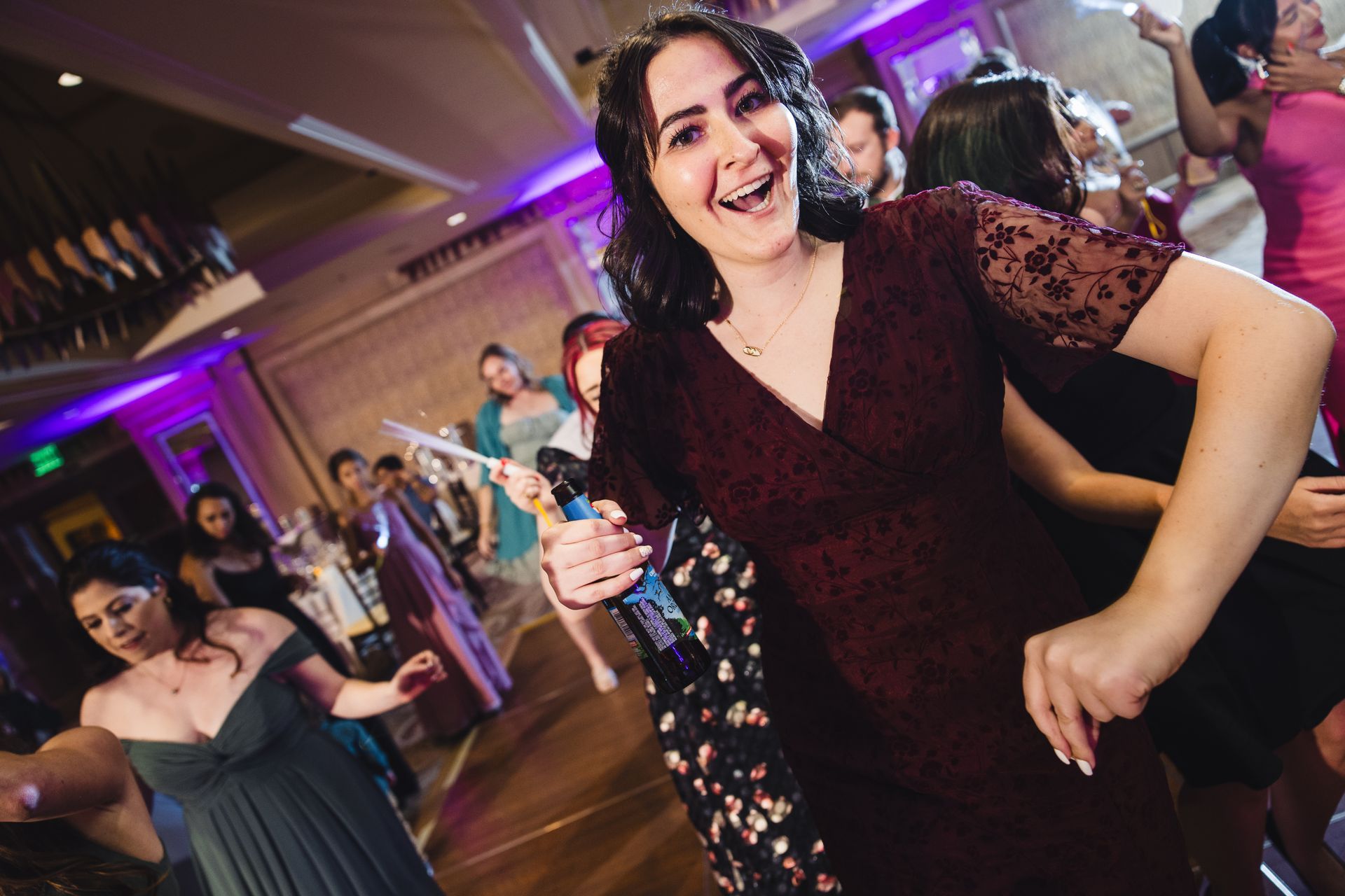 A group of people, including a woman in a burgundy dress, dancing and celebrating at an event.