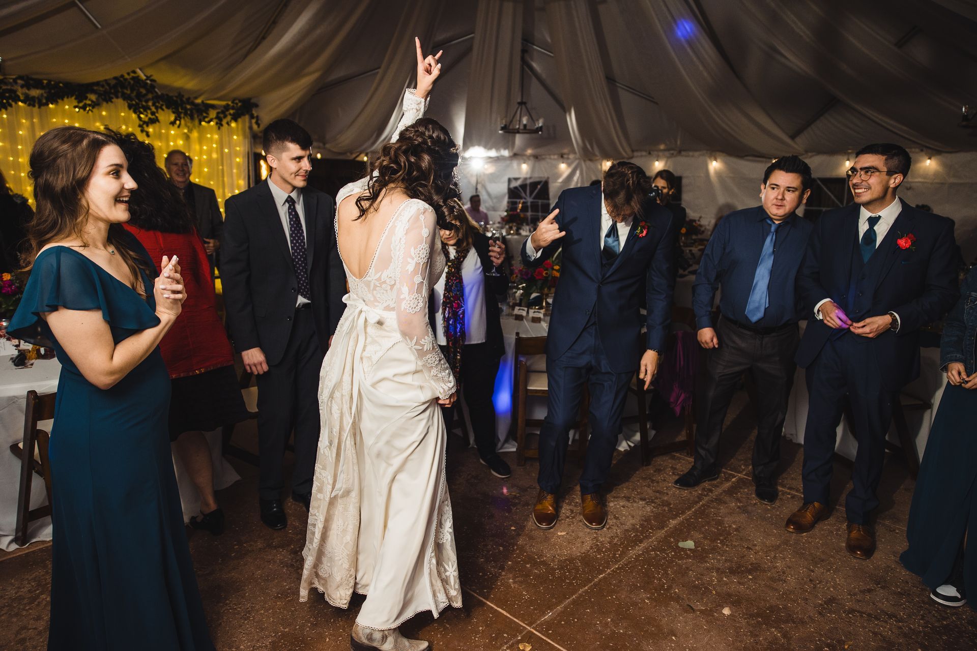Bride dances with guests at a wedding reception; a man bends backward.