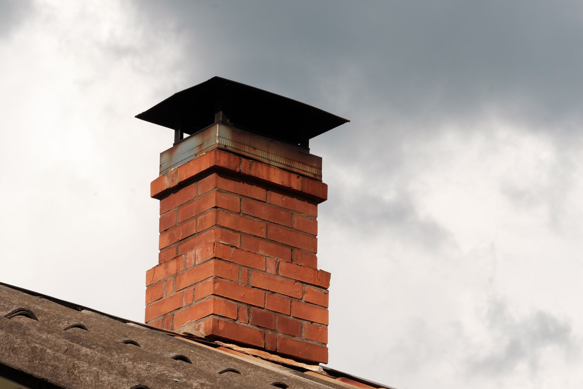 A brick chimney on top of a roof with a cloudy sky in the background.