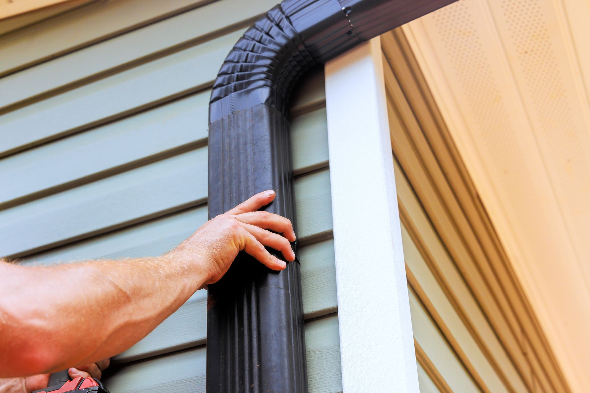 A man is installing a gutter on the side of a house.