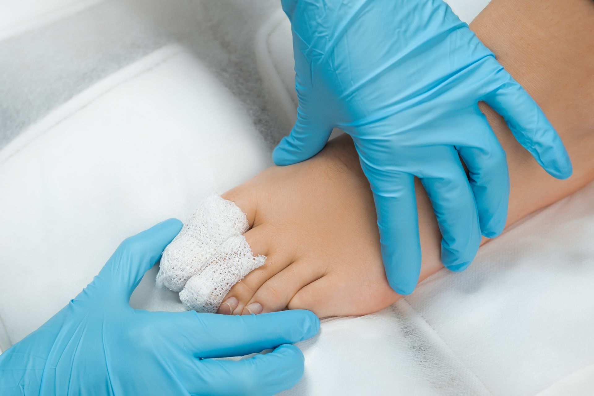Gloved hands treating a foot injury with gauze wrapped around the patient’s toes.