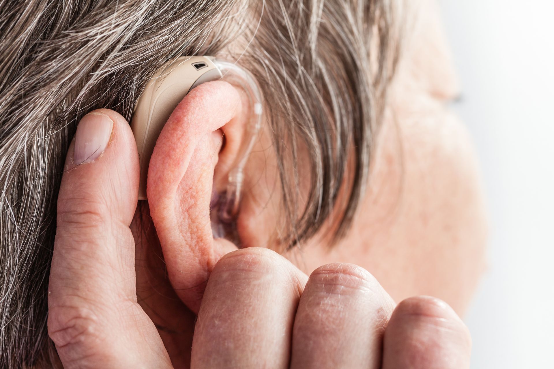 Close-up of a senior woman’s ear as she adjusts her hearing aid.