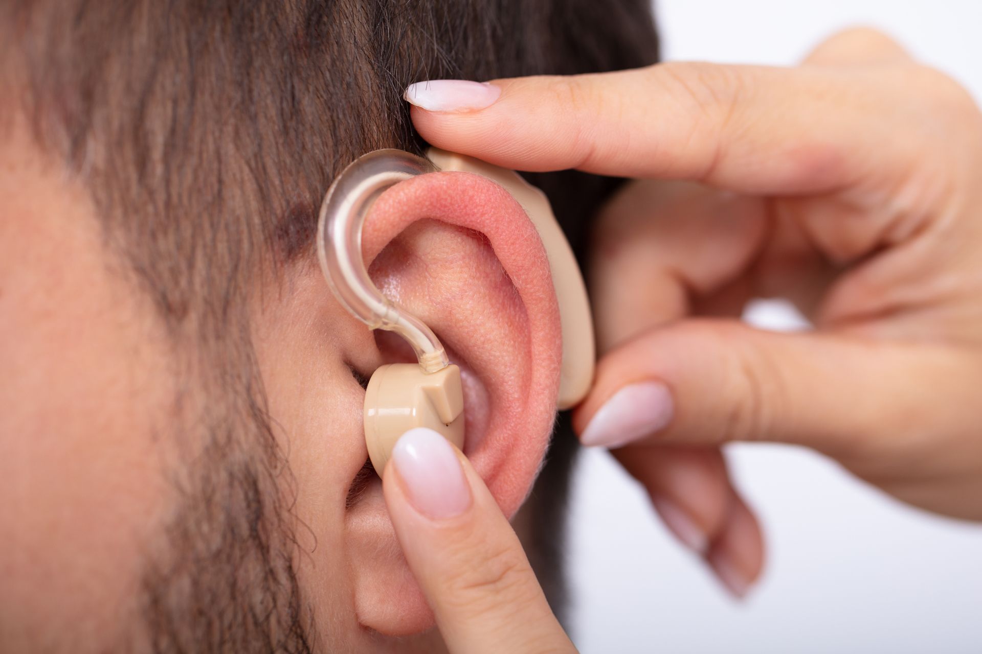 Person's ear with hearing aid being adjusted by a hand, indoor setting.