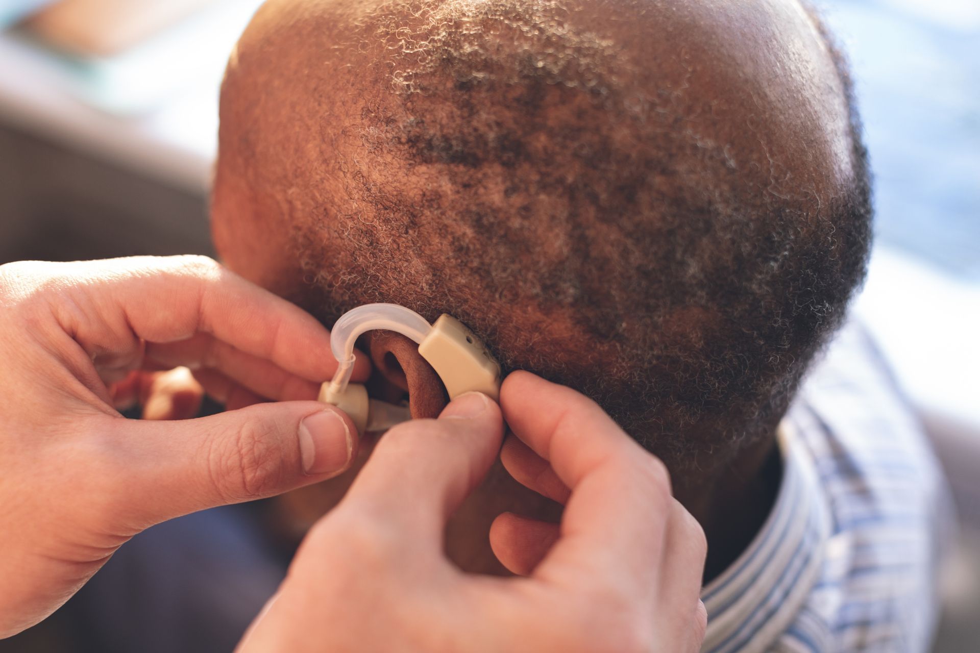 A Caucasian male doctor applying a hearing aid to a Black senior man's ear in a clinic.