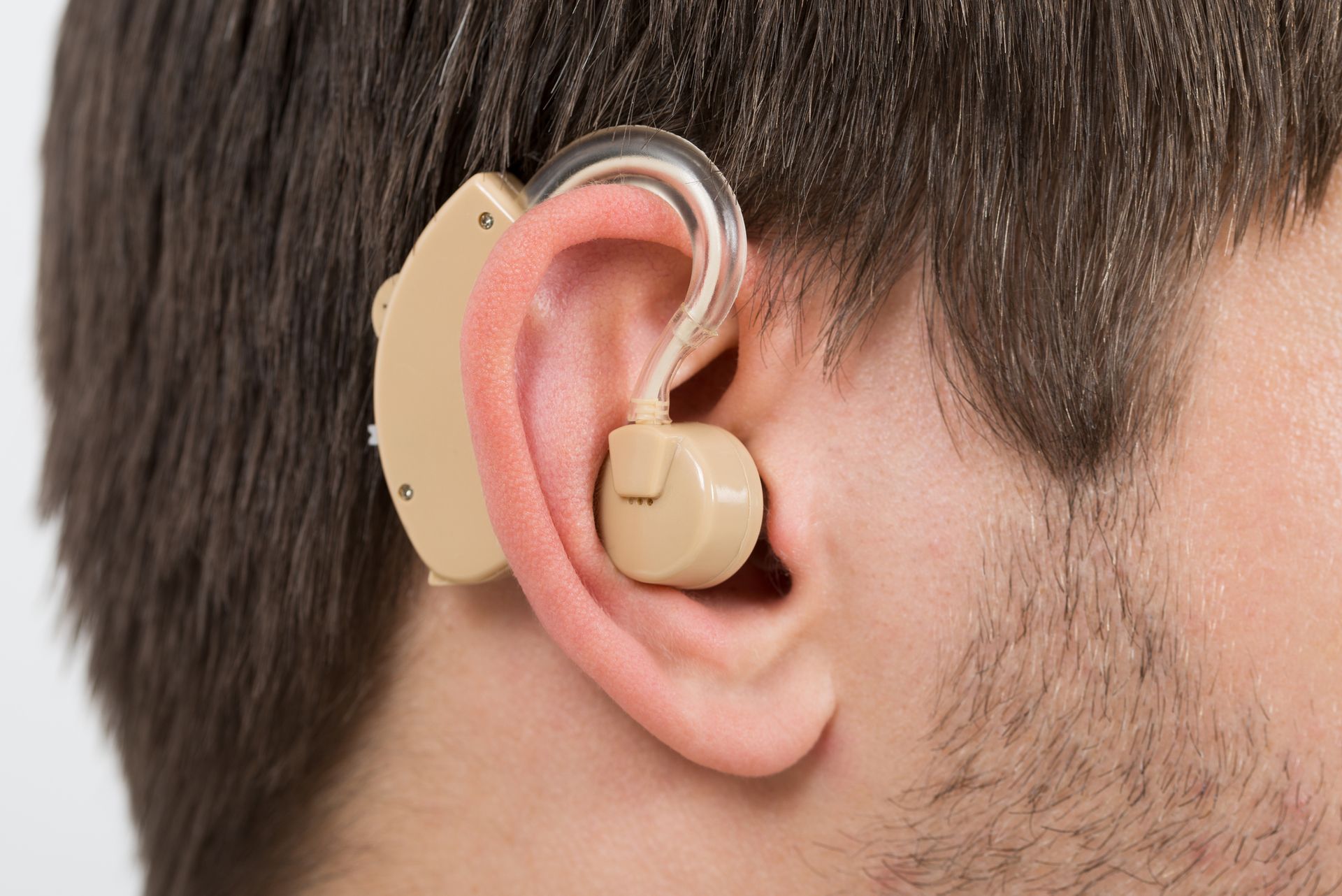 Close-up of ear wearing beige behind-the-ear hearing aid for hearing assistance.