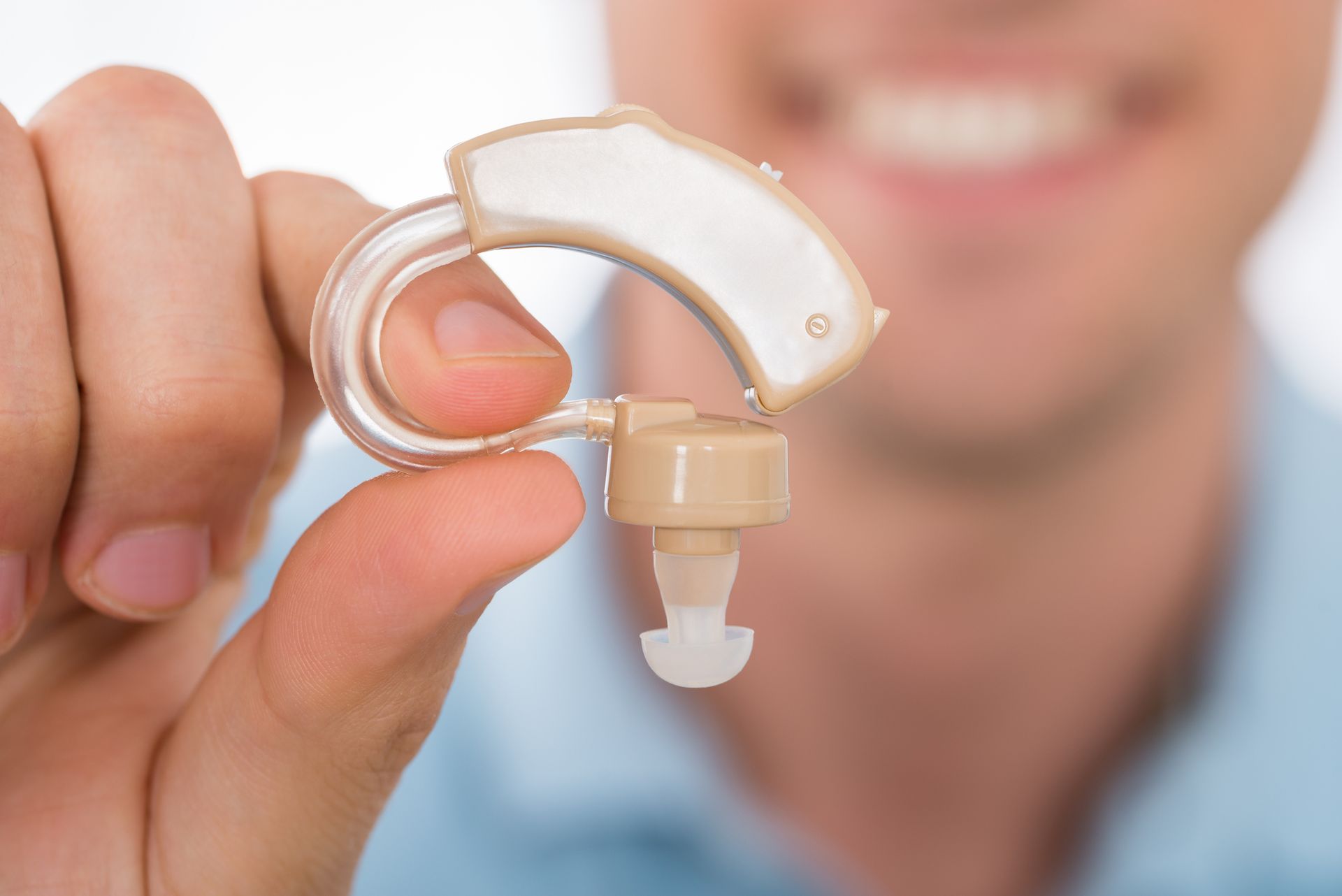 Person holding beige behind-the-ear hearing aid for hearing loss assistance.
