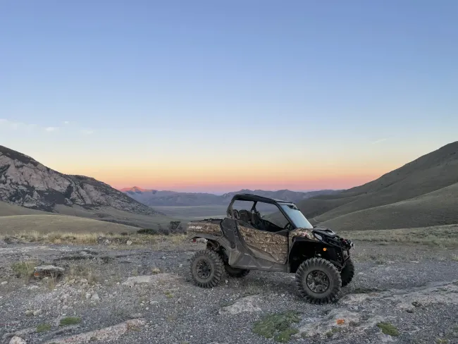 Side-by-side ATV on a gravelly hilltop, overlooking a valley at dusk.