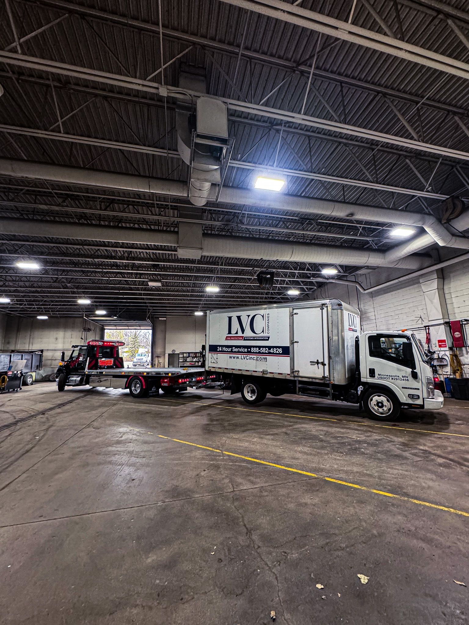 A white truck with trailer inside a large warehouse; a red truck on the left side.