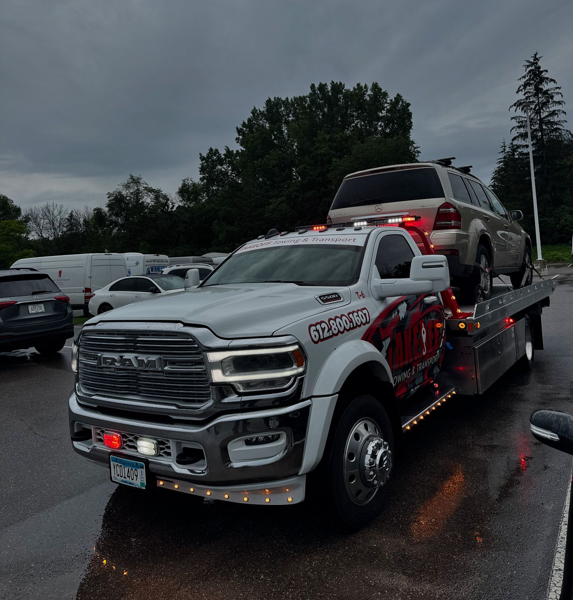 Tow truck with a car loaded on the flatbed, parked outside, cloudy sky.