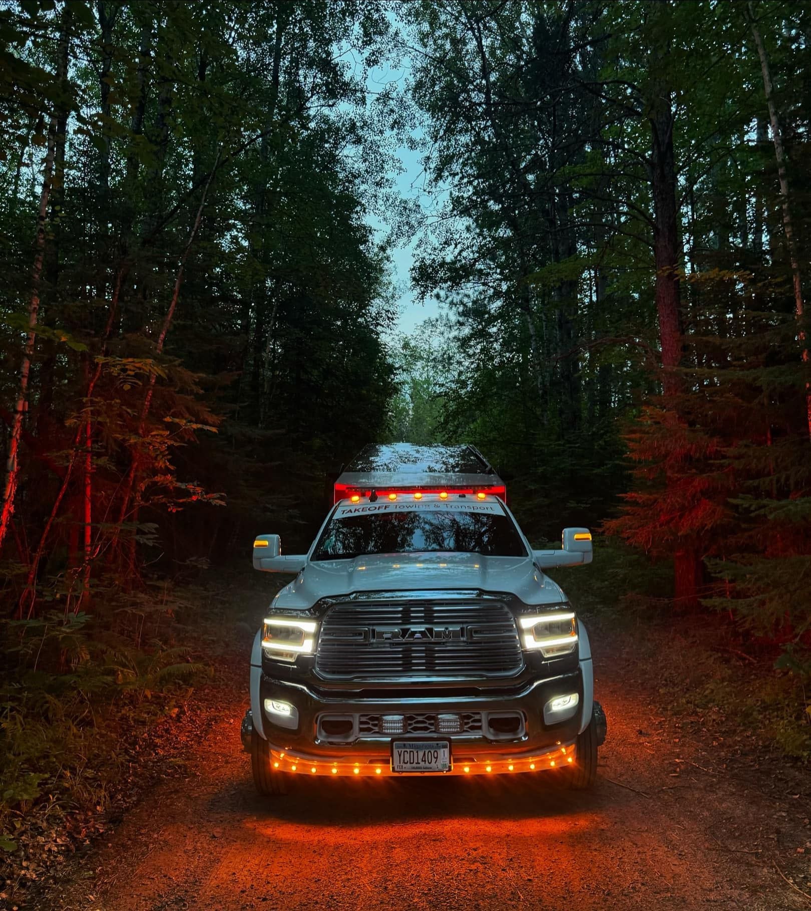 White Ram truck with orange lights on a dark forest road.