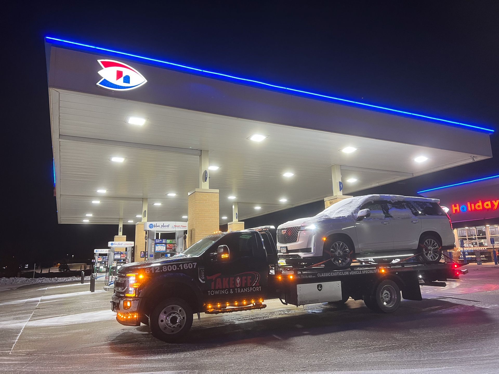Tow truck with a car loaded at a gas station at night.