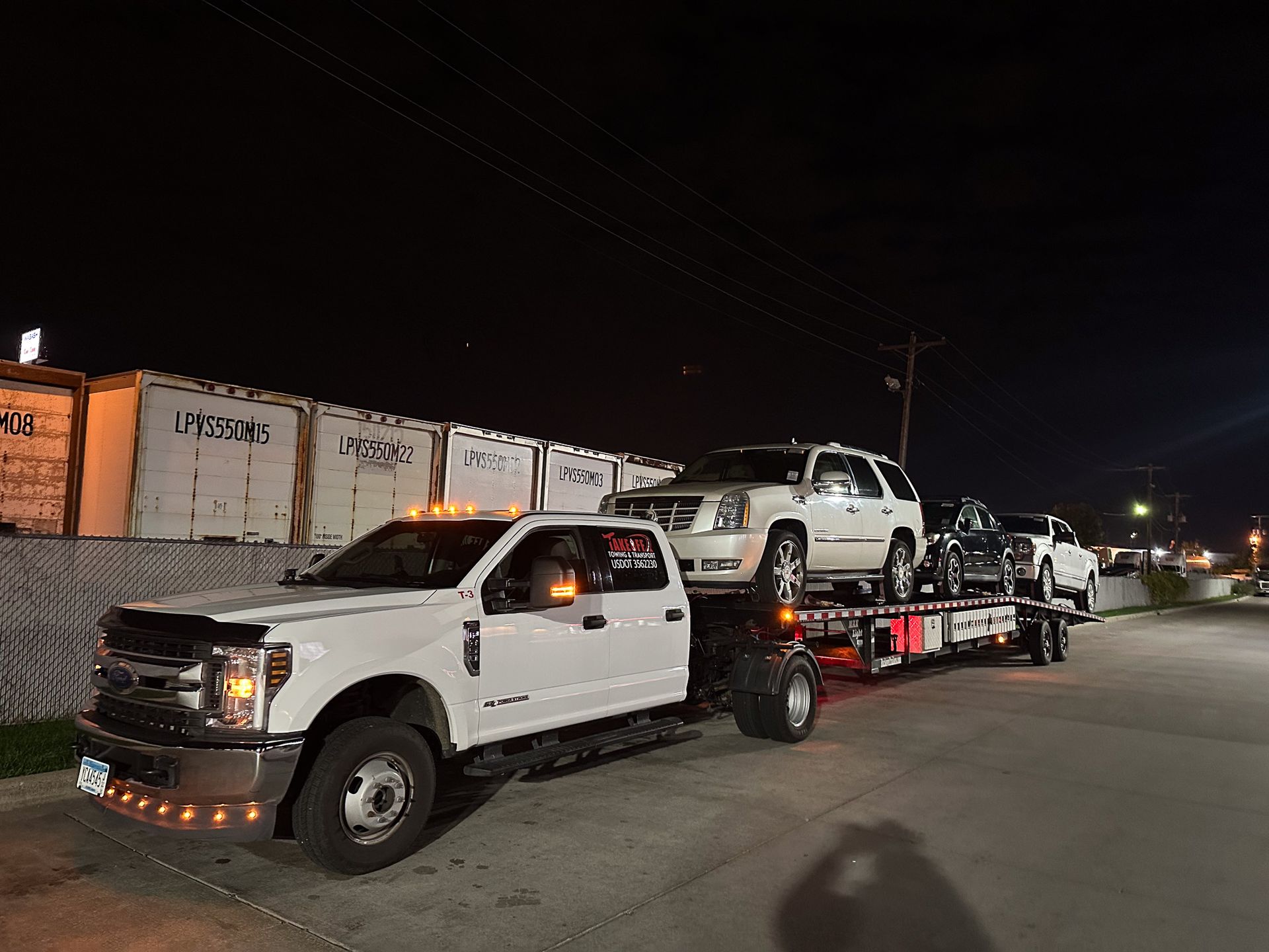 White truck towing three vehicles at night.