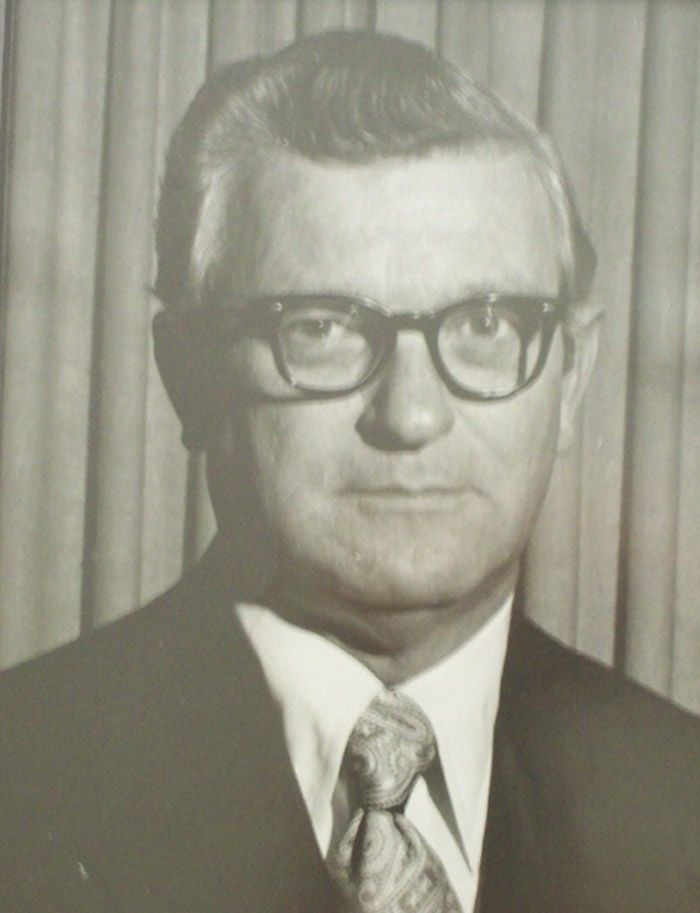 Man wearing glasses, suit, and tie, looking forward in a studio portrait.