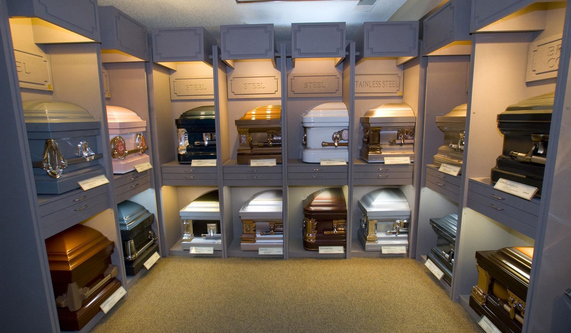 Display of various caskets in a funeral home showroom. They are housed in illuminated alcoves.