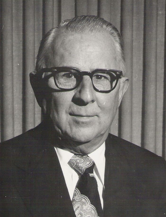 Man in glasses, suit and tie, facing forward, appears to be a formal portrait.