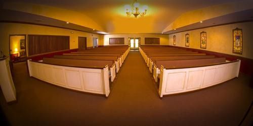Interior view of a chapel with rows of wooden pews and arched ceiling.