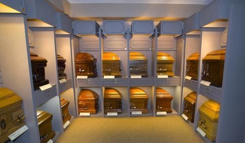 Caskets displayed in lighted wall niches in a room, varying colors and styles.