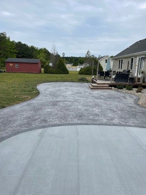 Concrete patio in backyard. Gray stamped concrete area with green grass and red shed. Cloudy sky.