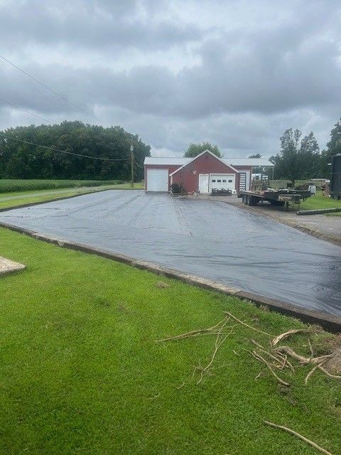 Paved driveway in front of a red building with two garage doors; green grass surrounds the driveway; cloudy sky overhead.