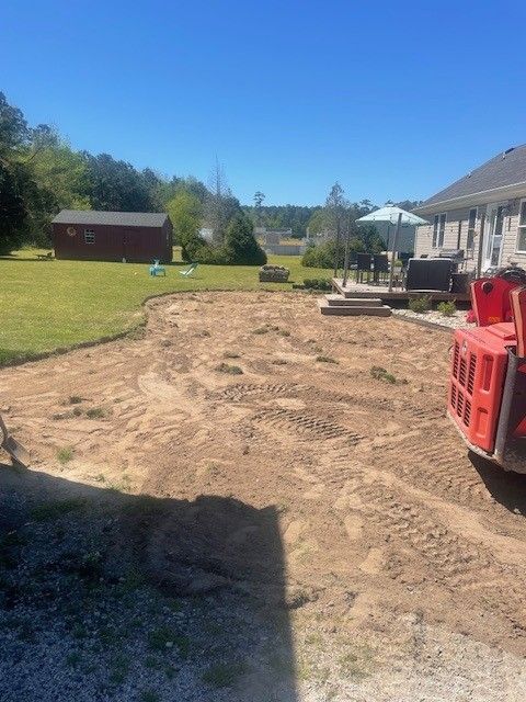 A backyard with cleared dirt ready for landscaping. A red machine sits on the right. A shed is in the distance.