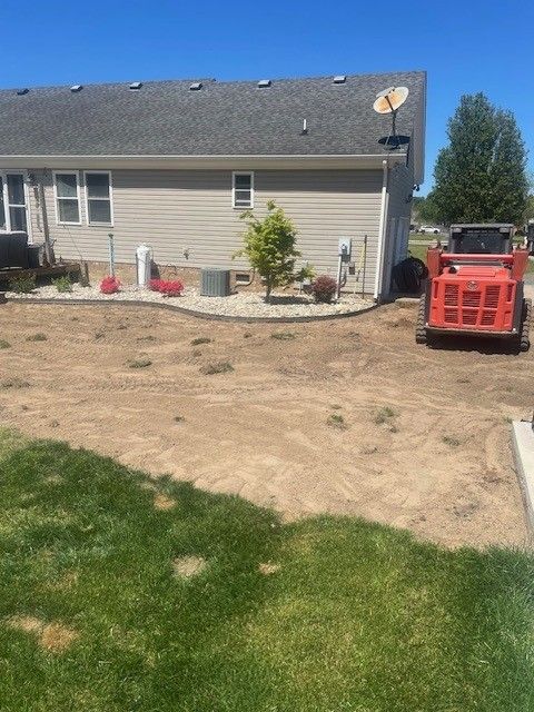 A small, orange skid steer next to a house with a dirt area and green grass.