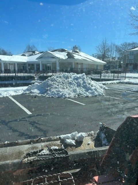 Snow pile in a parking lot with a building in the background under a blue sky.