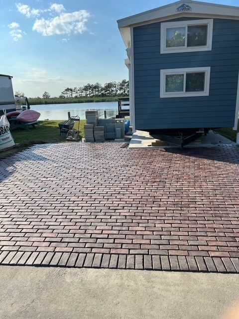 Brick patio in front of a blue house with a lake view, building materials nearby.