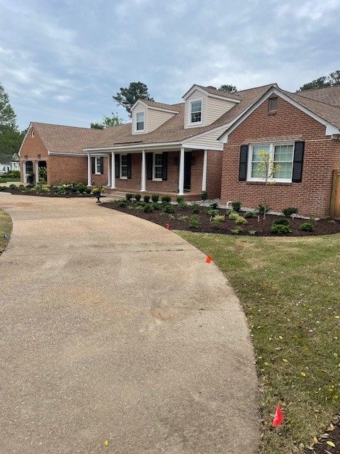 Brick house with concrete driveway and newly planted landscaping. Cloudy sky.