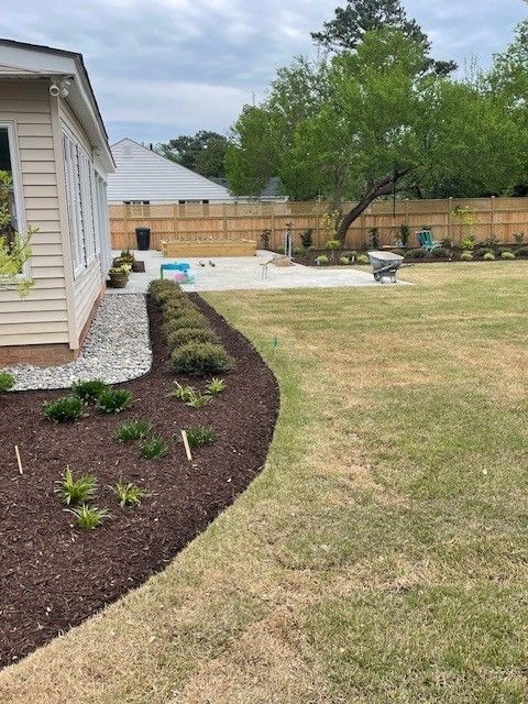 Backyard with landscaped flowerbeds, lawn, patio, and light beige house.