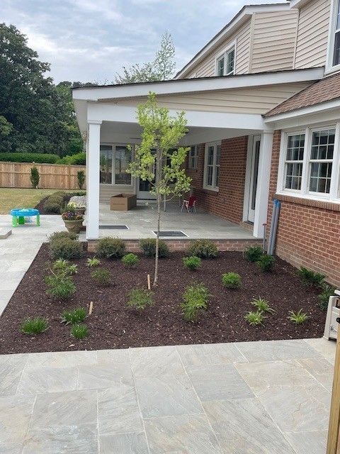 Backyard with new landscaping, brick house, and covered porch.