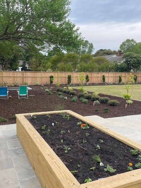 Raised garden bed with plants, freshly mulched beds, and wooden fence in the background.